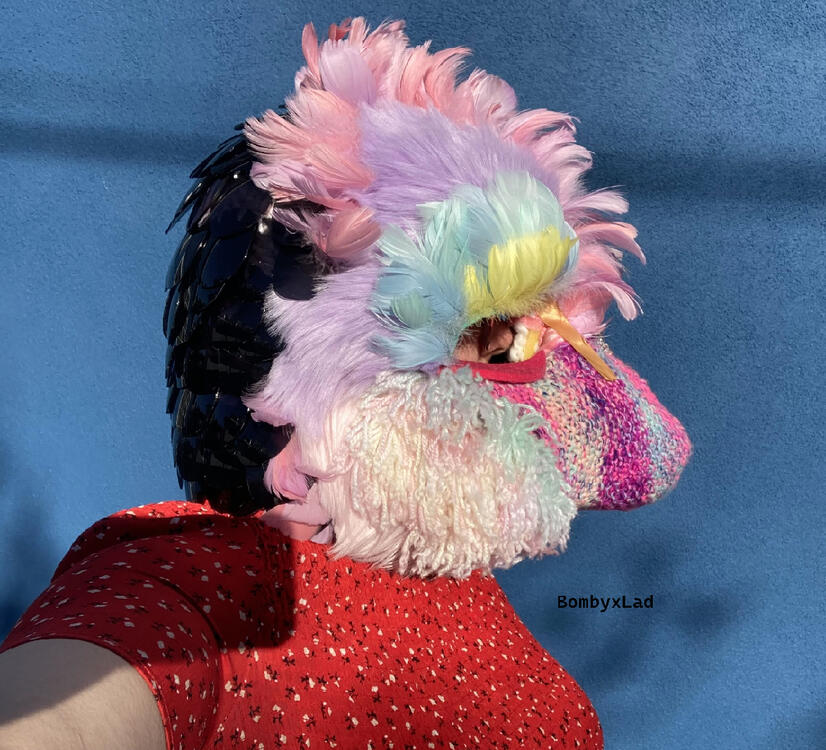 pangolin head side, being worn, it's pink with yarn and feathers